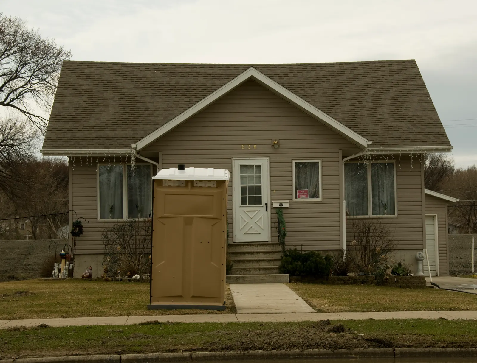 A portable toilet unit standing on the verge outside a single-storey house